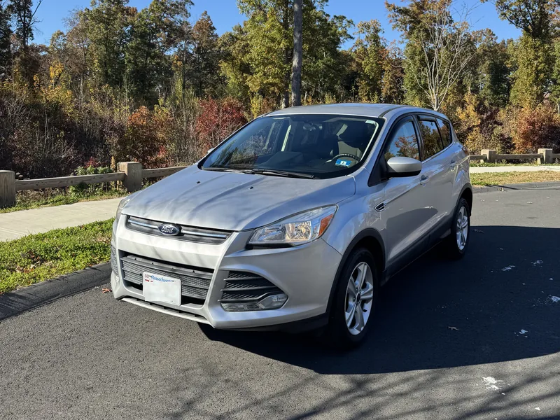 Silver Ford Escape SUV, front three-quarter view, parked by autumn trees