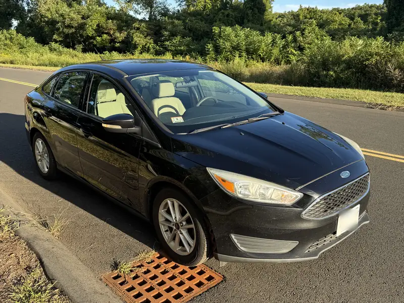 Black Ford Focus sedan, front three-quarter view, parked at the roadside in evening light