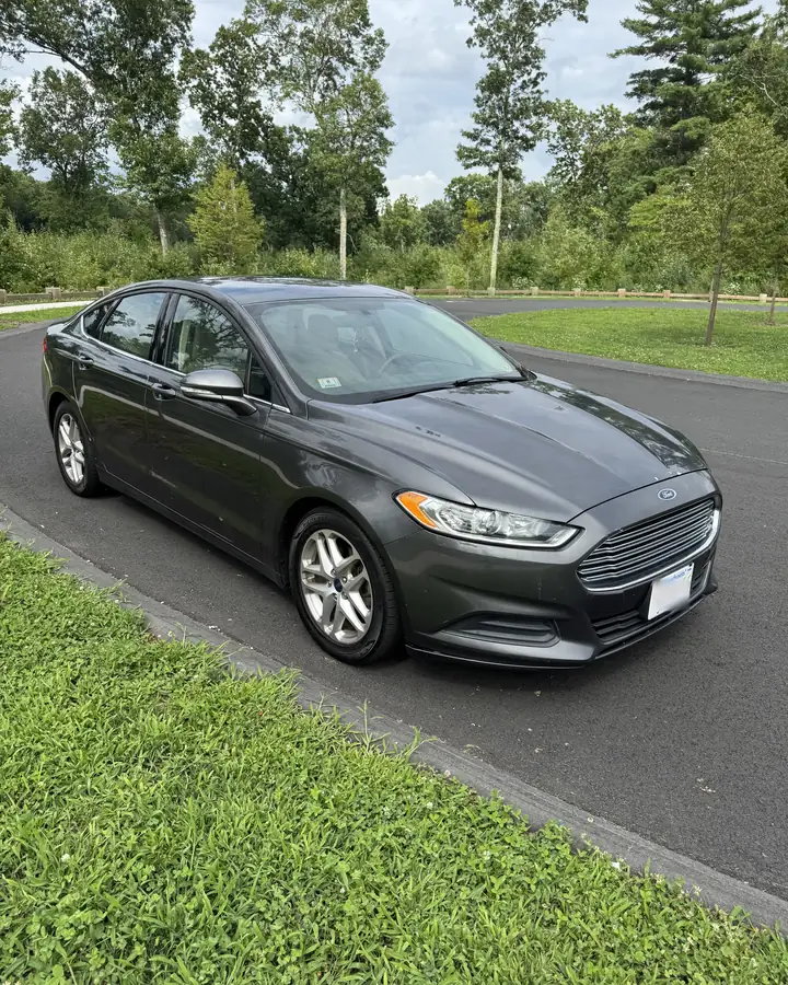 Grey Ford Fusion sedan from Exklusive Rentals, parked on a tree-lined road